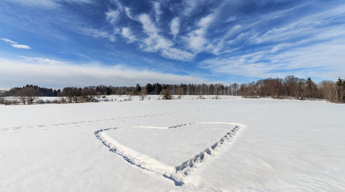 Heart shape on snow covered field against sky