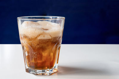A glass of cola with ice on a white table close-up. cold refreshing drink