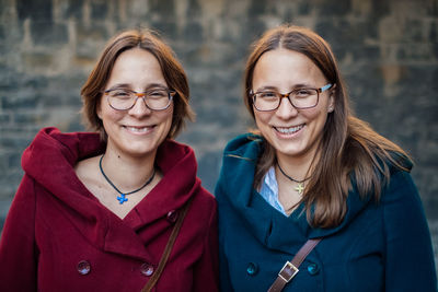 Portrait of smiling sisters standing against stone wall