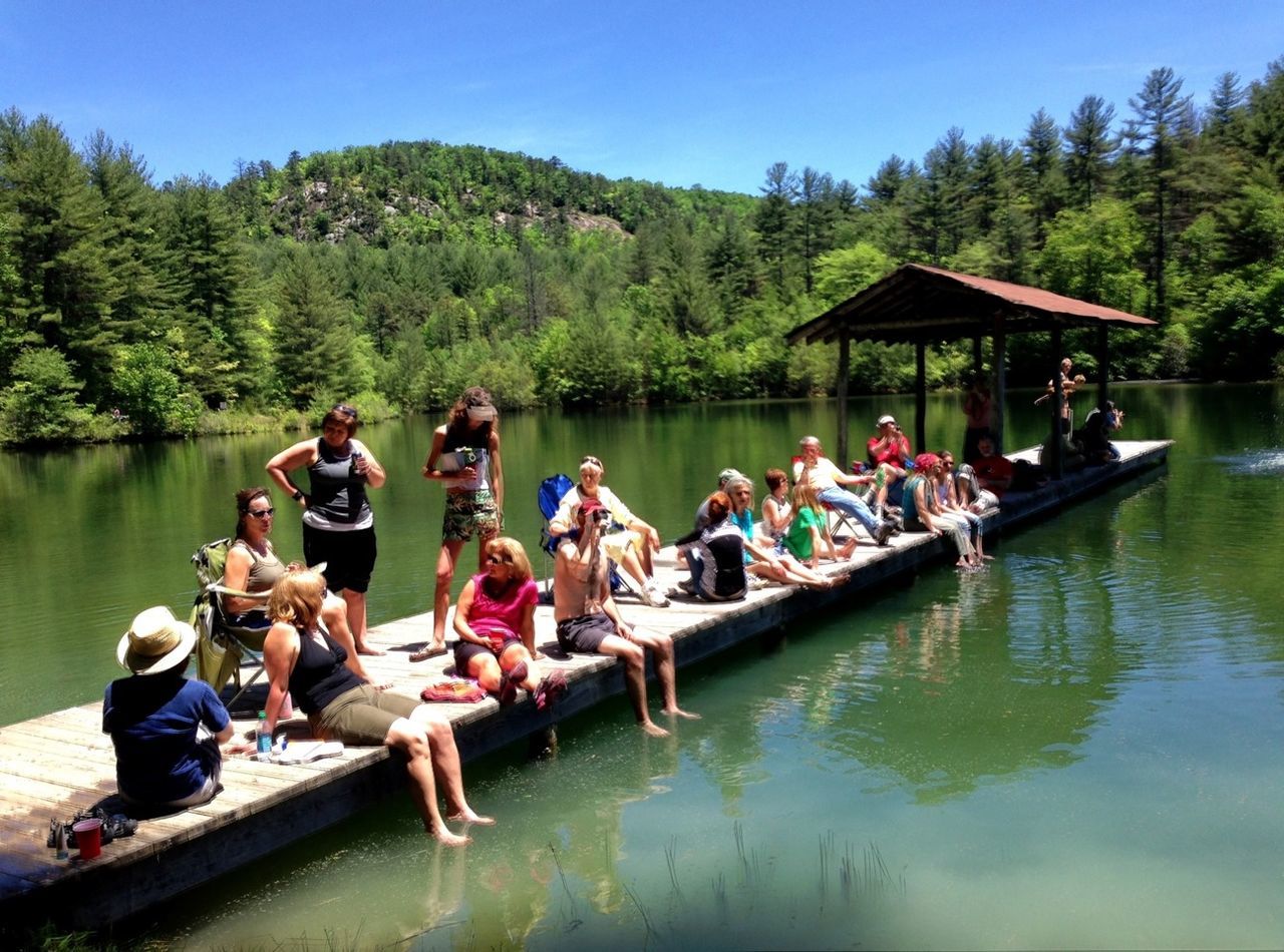 water, tree, waterfront, lake, reflection, nautical vessel, men, transportation, river, large group of people, lifestyles, person, mode of transport, leisure activity, boat, nature, day, built structure, tranquility