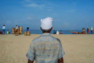 Rear view of fisherman standing at beach against sky