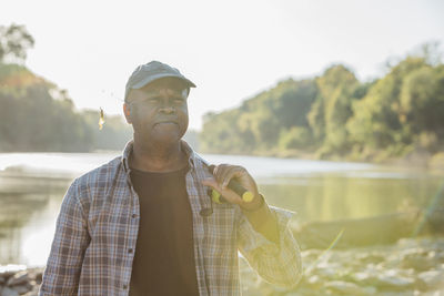 Man holding fishing rod looking away while standing at lakeshore