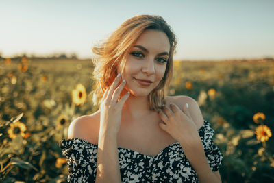 Portrait of young woman standing amidst plants on field