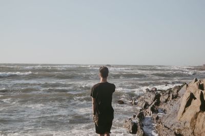 Rear view of man standing at beach against clear sky