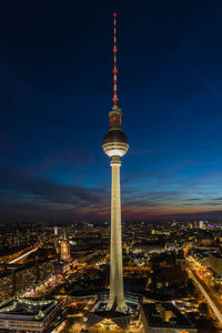 Illuminated fernsehturm against cloudy sky at dusk