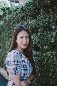 Portrait of smiling young woman standing against trees