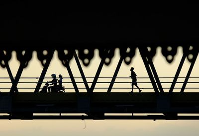Silhouette people working on bridge against clear sky