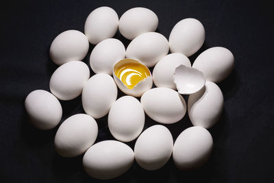 White chicken eggs with one broken egg on a black background