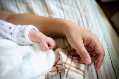 Cropped hand on mother and baby sleeping on bed