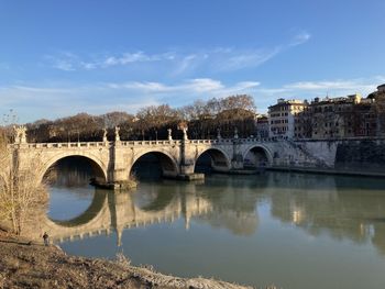 Arch bridge over river by buildings against sky