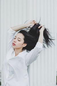 Beautiful woman with hand in hair against white wall