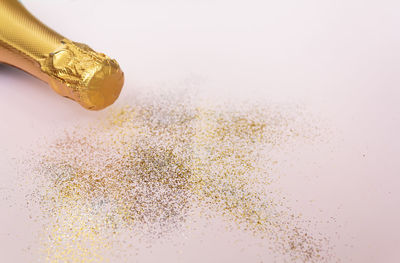 Golden champagne bottle and glitter on pink background with copy space. celebration concept