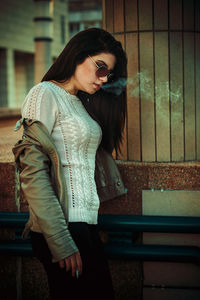 Young woman smoking while standing on street in city