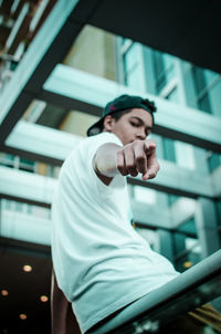 Portrait of man pointing while sitting on railing by building