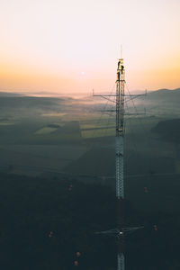 People on electricity pylon over landscape against sky during sunset