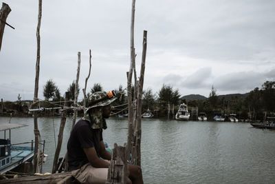 Side view of man sitting by river against sky