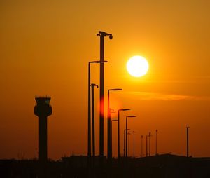 Silhouette street lights against orange sky during sunset