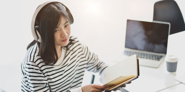 Woman looking away while sitting with book at desk