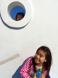 Portrait of smiling boy peeking from hole with girl hiding by wall