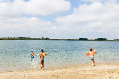 Boys with water wings running at beach against sky