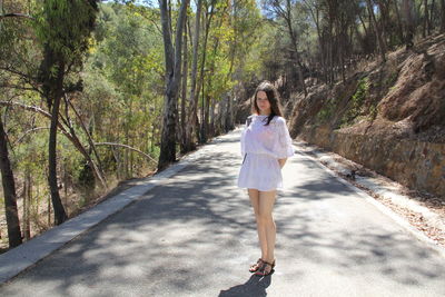 Portrait of woman standing on road amidst trees in forest