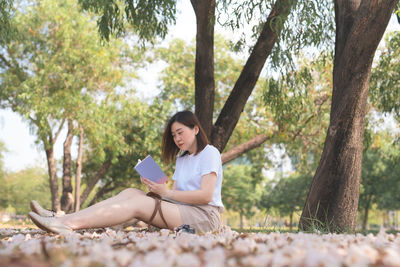 Young woman sitting on tree trunk against plants