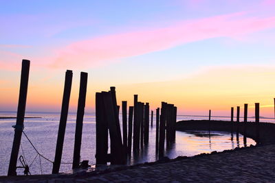 Silhouette wooden posts on sea against sky during sunset