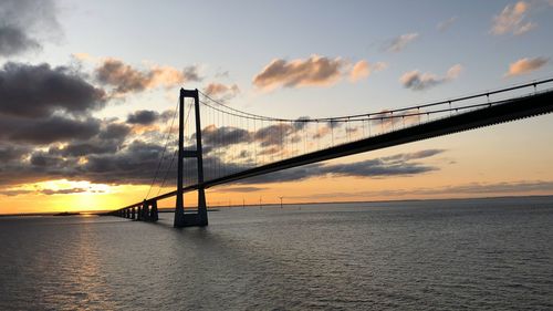 Silhouette bridge over sea against sky during sunset