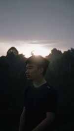 Young man looking away against sky during sunset