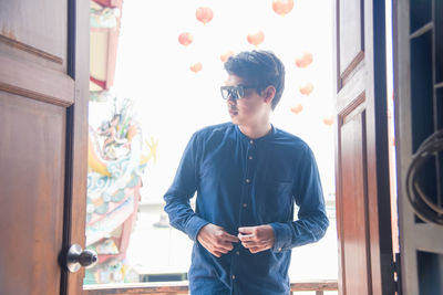 Young man wearing sunglasses standing in balcony seen through doorway