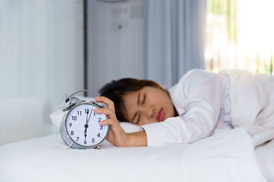 Woman holding alarm clock while sleeping on bed at home