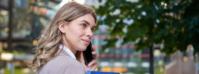 Portrait of young woman looking away against trees