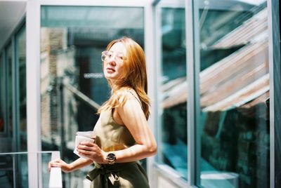 Young woman using mobile phone while standing in mirror