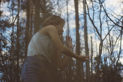 Low angle view of young woman dancing in forest