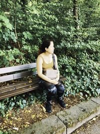 Side view of a woman sitting on plant in forest