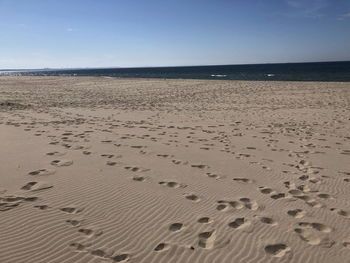 Footprints on sand at beach against clear sky