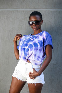 Portrait of a young woman wearing sunglasses standing against wall