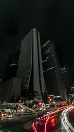 Illuminated city street by buildings against sky at night