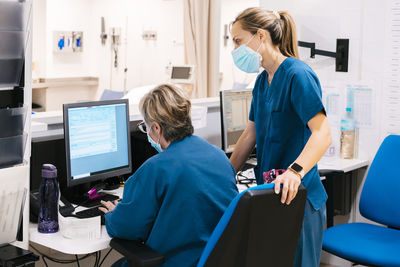 Mature nurse with colleague discussing over computer at hospital