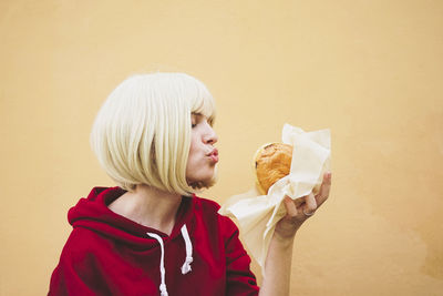 Woman puckering at hamburger in front of peach wall