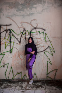 Portrait of young woman standing against wall