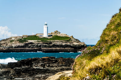 Lighthouse on cliff by sea against sky