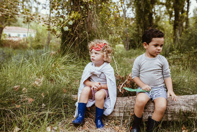 Cute boys wearing boots sitting on log in forest