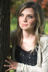 Thoughtful woman standing by tree trunk