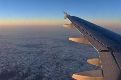 Cropped image of airplane wing flying over cloudscape during sunset