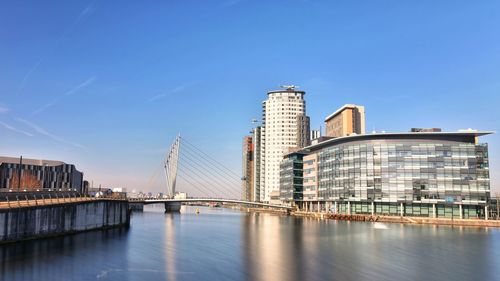 Bridge over river by buildings against blue sky