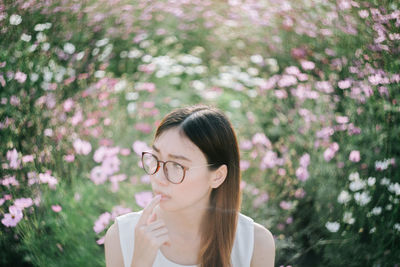 Thoughtful young woman wearing eyeglasses looking away against flowers