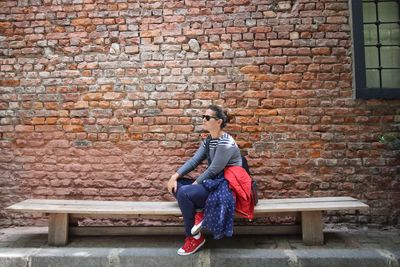 Young woman sitting against brick wall