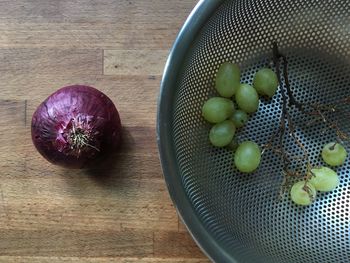 Directly above shot of grapes in strainer by onion on table