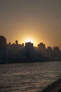 Sea by cityscape against sky during sunset